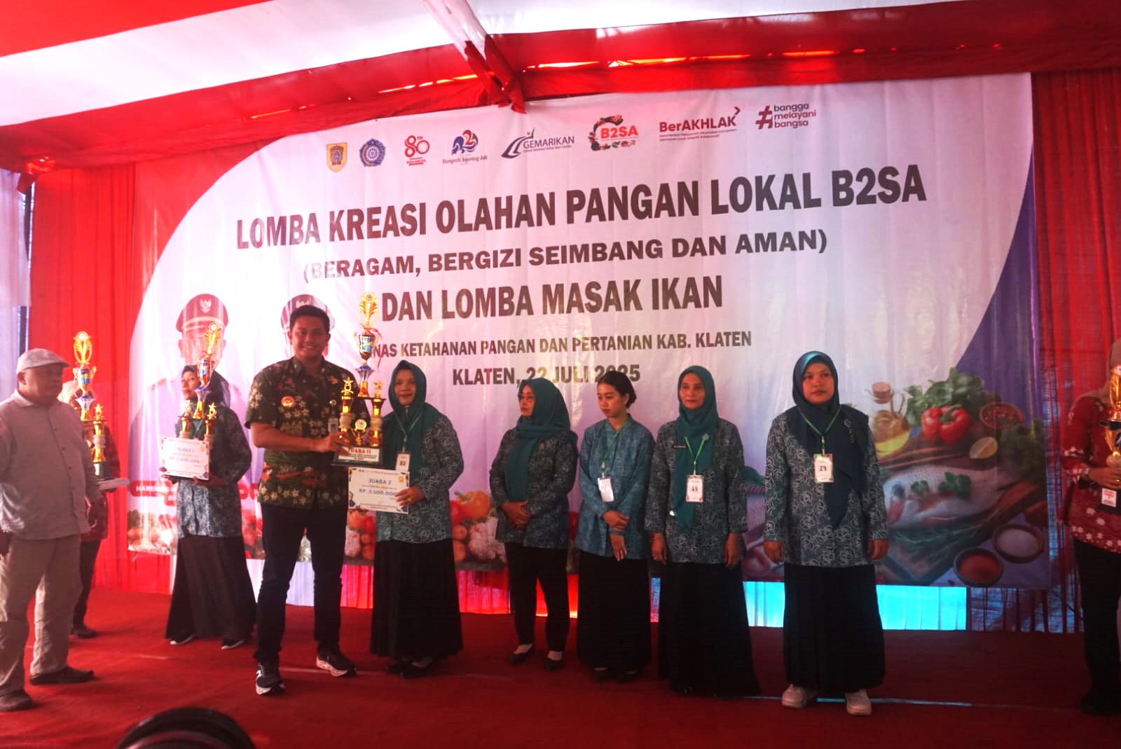 Bupati Klaten Hamenang Wajar Ismoyo saat menyerahkan piala saat memberikan piala kepada peserta lomba masak ikan dan olahan pangan lokal B2SA di halaman Kantor DKPP Klaten, Selasa (22/7/2025).