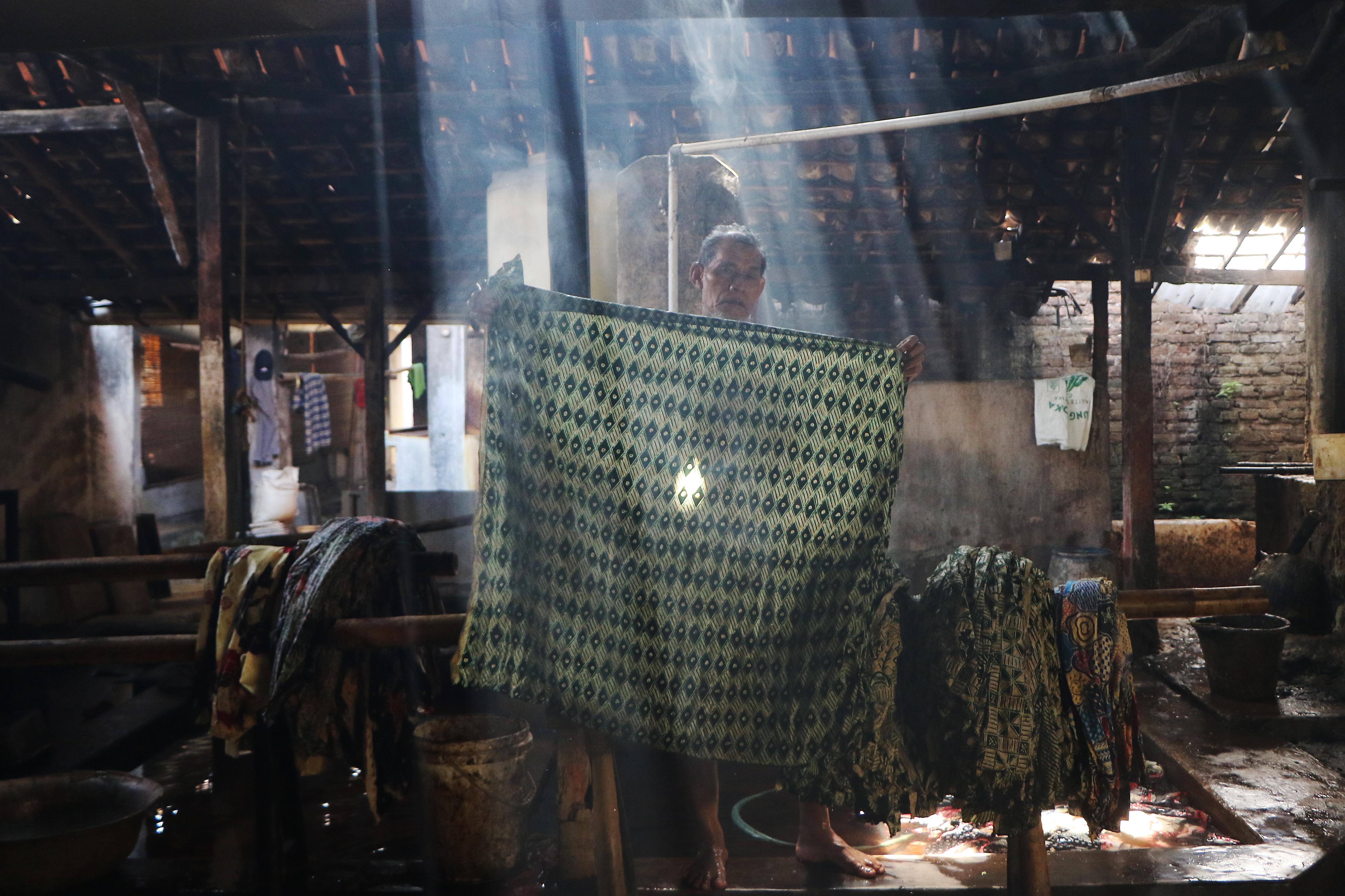 Ilustrasi pekerja membilas kain batik yang menggunakan pewarna alami. Memperingati Hari Batik Nasional, akan digelar Solo Batik Fashion 2025 pada 3-5 Oktober.