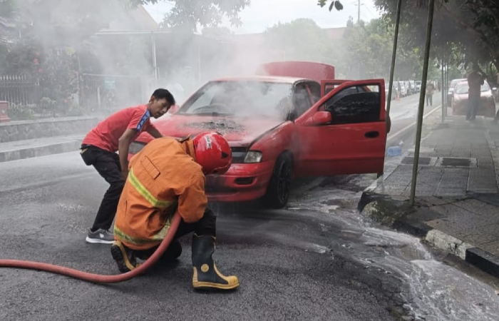 Petugas damkar melakukan pemadaman dan pendinginan pada mobil yang terbakar.