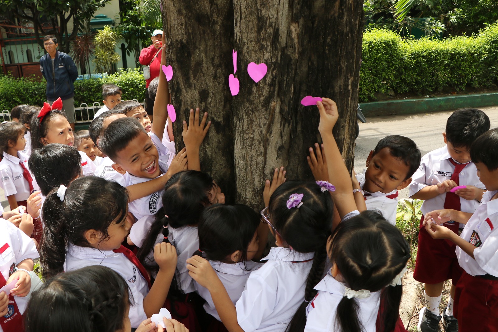 CINTA LINGKUNGAN: Siswa sekolah dasar di kawasan Manahan ini memberi simbol cinta lingkungan dengan memeluk pohon dan memasang tanda cinta, Senin (1/12/2025).