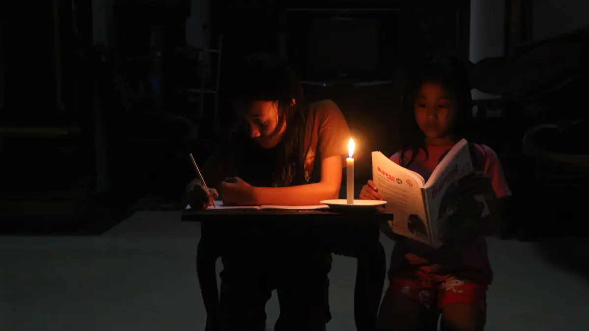Dua orang anak tengah belajar dengan bantuan lilin, saat adanya kebijakan listrik tengah mati. (Arief Budiman/Radar Solo)