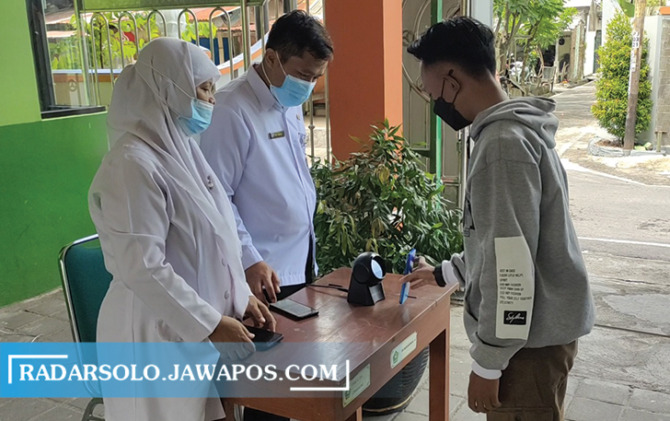 MINIM INTERAKSI: Orang tua siswa MTsN 2 Surakarta men-scan barcode ke alat presensi pintar ramah pandemi, saat hendak menjemput buah hatinya di gerbang sekolah. (SEPTIAN REFVINDA/RADAR SOLO)