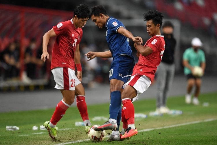Bek tengah indonesia Alfeandra Dewangga Santosa (kiri) dan bek kiri Pratama Arhan mencoba merebut bola dari kaki striker Thailand Teerasil Dangda pada leg kedua final AFF Cup 2020. Kedua pemain tim nasional tersebut merupakan pemain PSIS Semarang. (Rosla