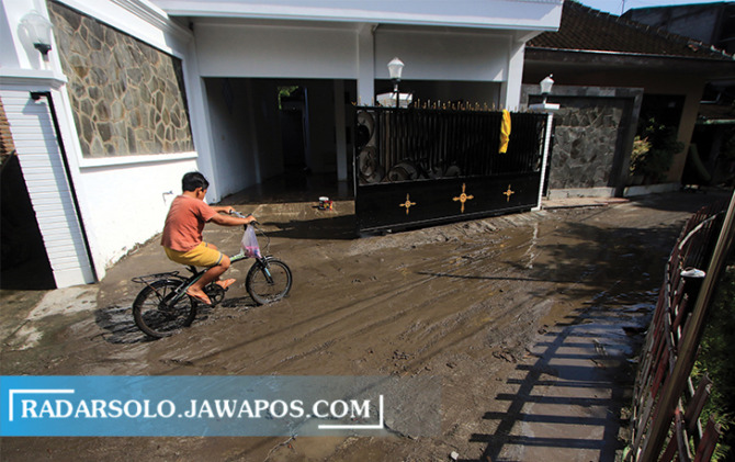 LICIN BERLUMPUR: Anak bersepeda melintasi lumpur sisa banjir di Pajang, Laweyan. Lokasi ini menjadi langganan tergenang saat hujan deras. (ARIEF BUDIMAN/RADAR SOLO)