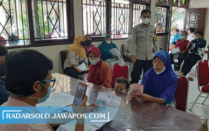 ANTRE: Warga dari keluarga penerima manfaat (KPM) mengambil bantuan langsung tunai minyak goreng, Rabu (13/4). (RAGIL LISTIYO/RADAR SOLO)