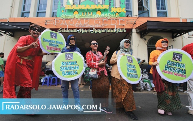 RAMAH: Warga membawa poster menyambut pemudik di Pasar Gede Solo, Minggu (1/5). Aksi tersebut selain menyambut pemudik juga dalam rangka memperingati hari tertawa sedunia serta mengajak pemudik untuk tertawa bersama. (ARIEF BUDIMAN/RADAR SOLO)