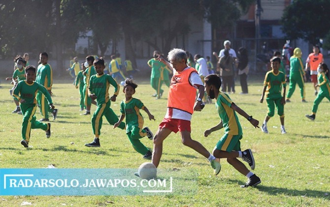 MENGHIBUR: Legenda Persis Solo era 1960 an Frans Setiabudi berebut bola dengan ratusan siswa SD dalam merayakan Hari Anak di Lapangan Sumber, (22/7). (ARIEF BUDIMAN/RADAR SOLO)