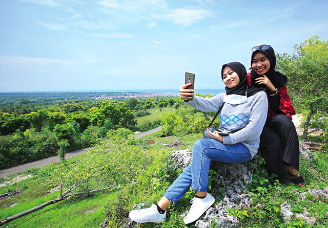 SELFIE DULU: Dua pengunjung Tebing Cafe berfoto bersama dengan latar belakang panorama wilayah pesisir. (Anjar Dwi/Jawa Pos Radar Lamongan)