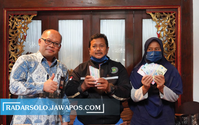 Samin, penjaga SDN Lojiwetan (tengah) bersama istri dan Kepala BI Solo Nugroho Joko Prastowo menunjukkan uang baru dari BI Solo, pengganti uang yang dimakan rayap, Kamis (15/9). (RIJAL H/RADAR SOLO)