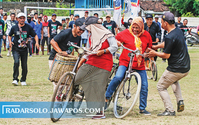 SERU: Emak-emak peserta balapan sepeda ontel bronjong sisih berhenti di tengah trek karena rok-nya tersangkut gir. (M. IHSAN/RADAR SOLO)