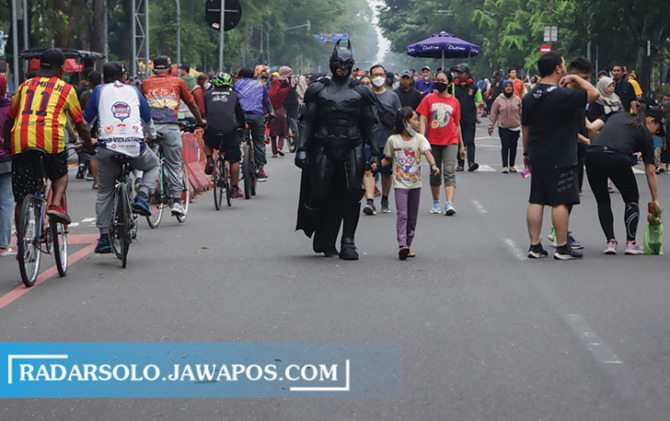 MENARIK PERHATIAN: Cosplayer berpakaian Batman tengah menggandeng anak kecil di momen CFD di Jalan Slamet Riyadi, Minggu pagi (1/1/2023). (M. IHSAN/RADAR SOLO)