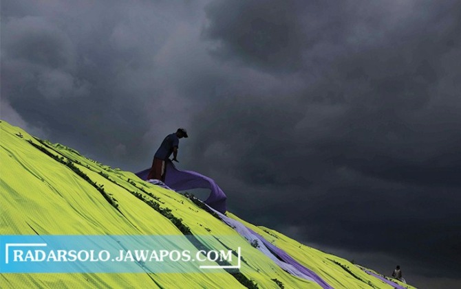 BEKEJARAN DENGAN HUJAN: Warga menjemur kain pantai di bantaran Bengawan Solo di Desa Krajan, Kecamatan Mojolaban, Sukoharjo dengan mendung gelap menggelayut di langit Kamis (26/1/2023). (ARIEF BUDIMAN/RADAR SOLO)