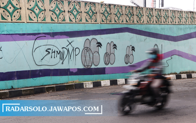 SASARAN: Pengendara motor melintas di Flyover Manahan yang terdapat coretan vandalisme, Senin (30/1/2023). (M. IHSAN/RADAR SOLO)