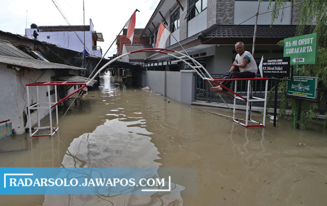 Seorang warga Joyotakan memilih bertahan di gapura kampung pasca banjir yang melanda rumah mereka, Jumat (17/2/2023). Hampir seluruh wilayah di Kelurahan ini terkena dampak dari banjir tersebut. (ARIEF BUDIMAN/RADAR SOLO)