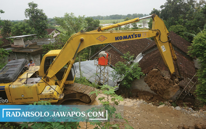 DIKEJAR WAKTU: Alat berat berupa ekskavator milik penambang sedang mengeruk material yang longsor menimpa dua rumah warga di Dusun Bomoten, Desa Ngandong, Kecamatan Gantiwarno. (ANGGA PURENDA/RADAR SOLO)
