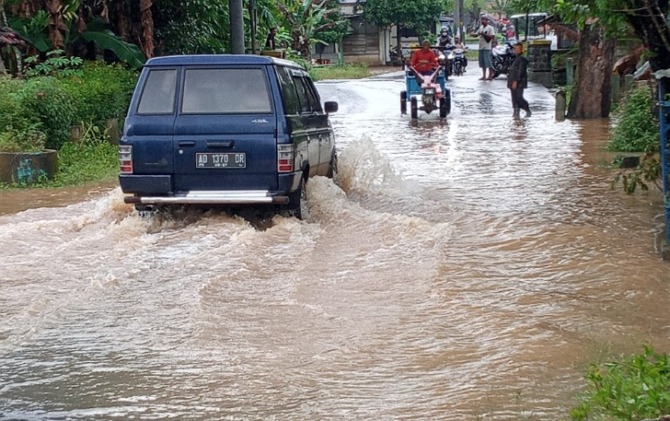 Luapan Sungai Wiroko yang menggenangi Jalan Raya Wonogiri-Tirtomoyo, Kamis (2/3) pagi. Ketinggian air yang mulai menyusut membuat sejumlah kendaraan berani menerjang banjir. (Istimewa)