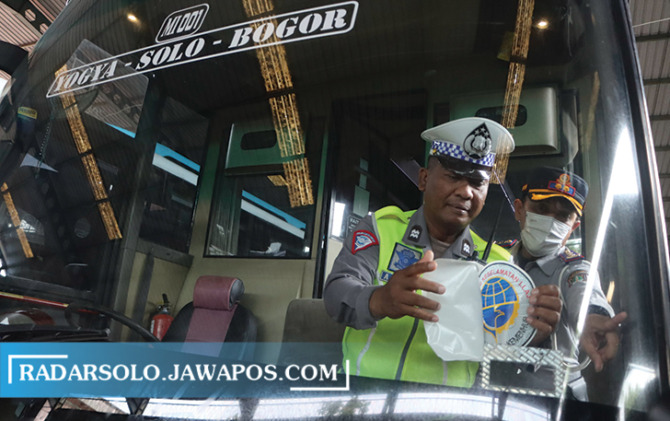 PASTIKAN AMAN: Petugas dishub menempeli stiker pada kaca bus angkutan Lebaran Kamis (13/4/2023). (M. IHSAN/RADAR SOLO)
