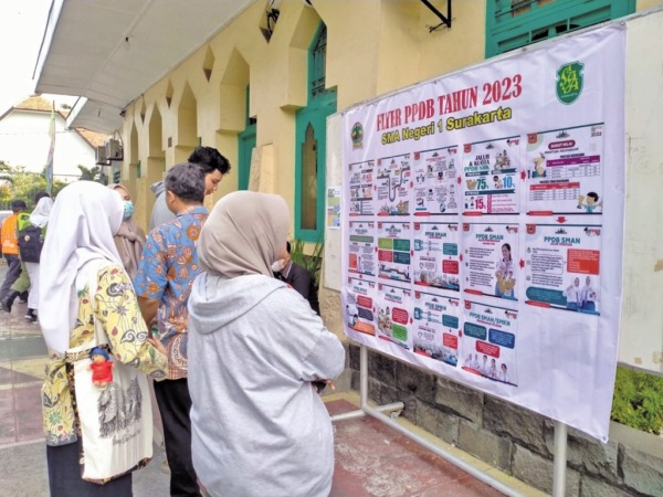 DICERMATI: Orang tua bersama calon peserta didik memerhatikan papan petunjuk proses pendaftaran penerimaan peserta didik baru di halaman SMAN 1 Surakarta, belum lama ini. (SEPTIAN REFVINDA/RADAR SOLO)