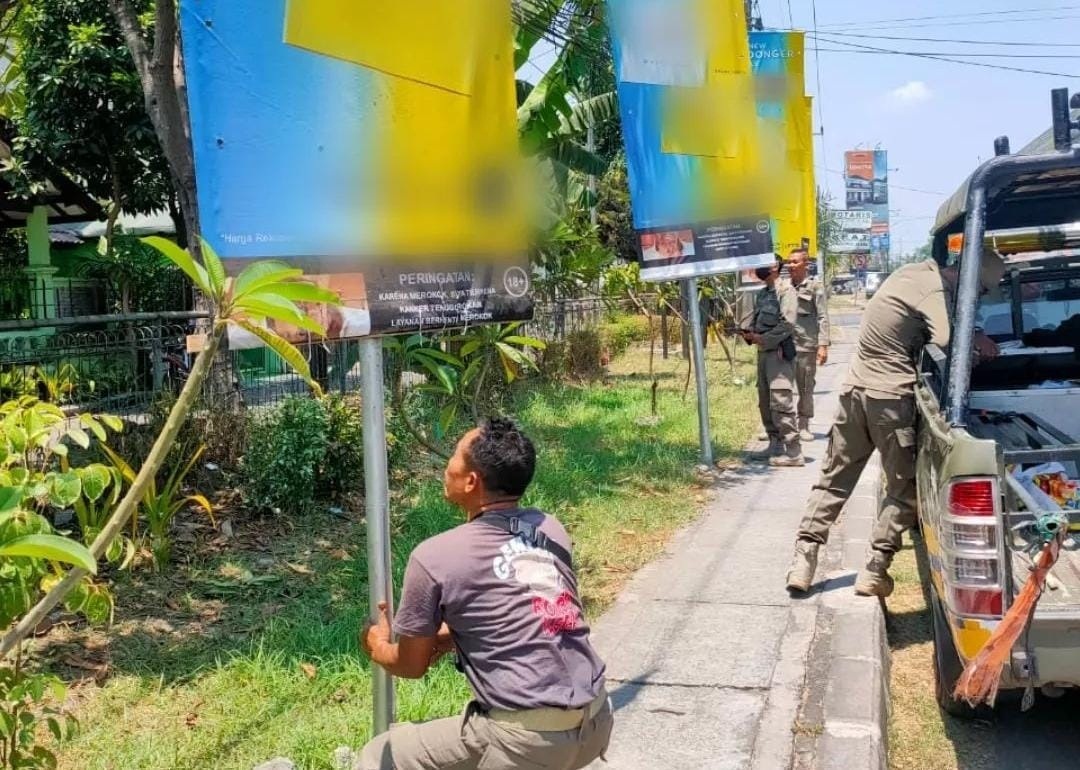 BERSIH: Petugas Satpol PP menurunkan reklame yang sudah habis pajak. (IST)