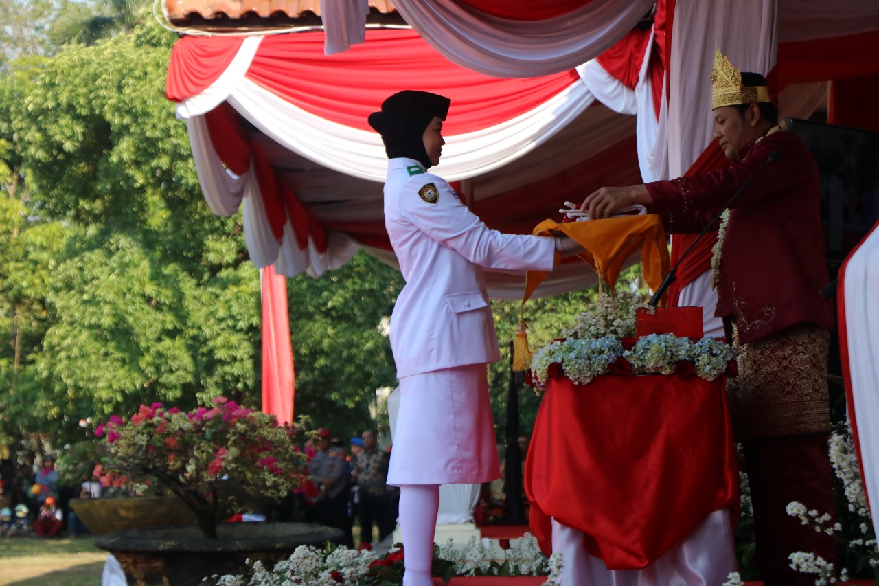 KHIDMAT : Plt Bupati Sidoarjo Subandi saat menyerahkan bendera merah putih untuk dikibarkan. (FOTO HUMAS DISKOMINFO)