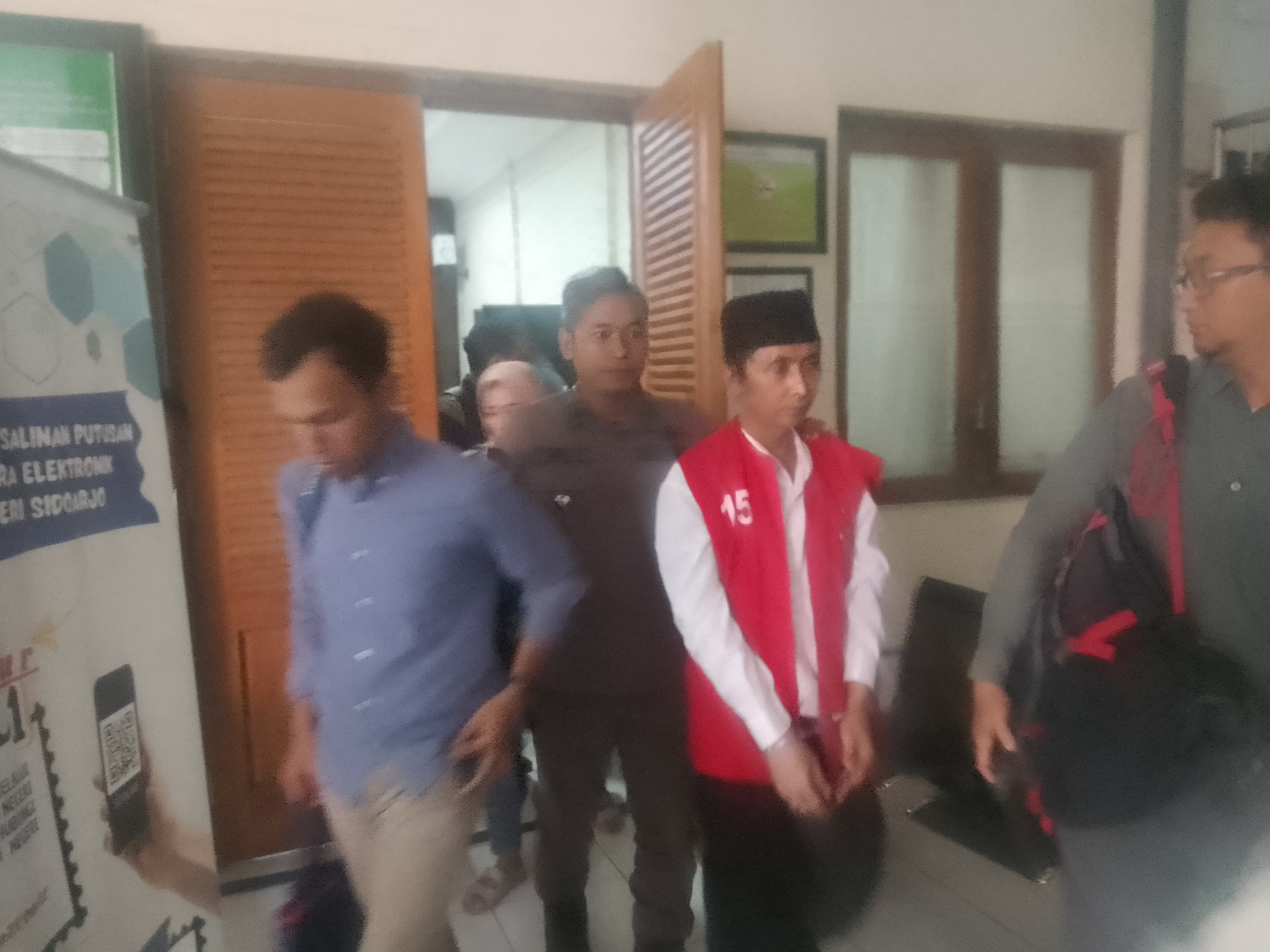 KESAKSIAN : Terdakwa Iyek (rompi merah) saat keluar dari ruang sidang PN Sidoarjo usai sidang kepemilikan SS sebanyak 30 kilogram, Kamis (20/2). (DIKY PUTRA SANSIRI/RADAR SIDOARJO)