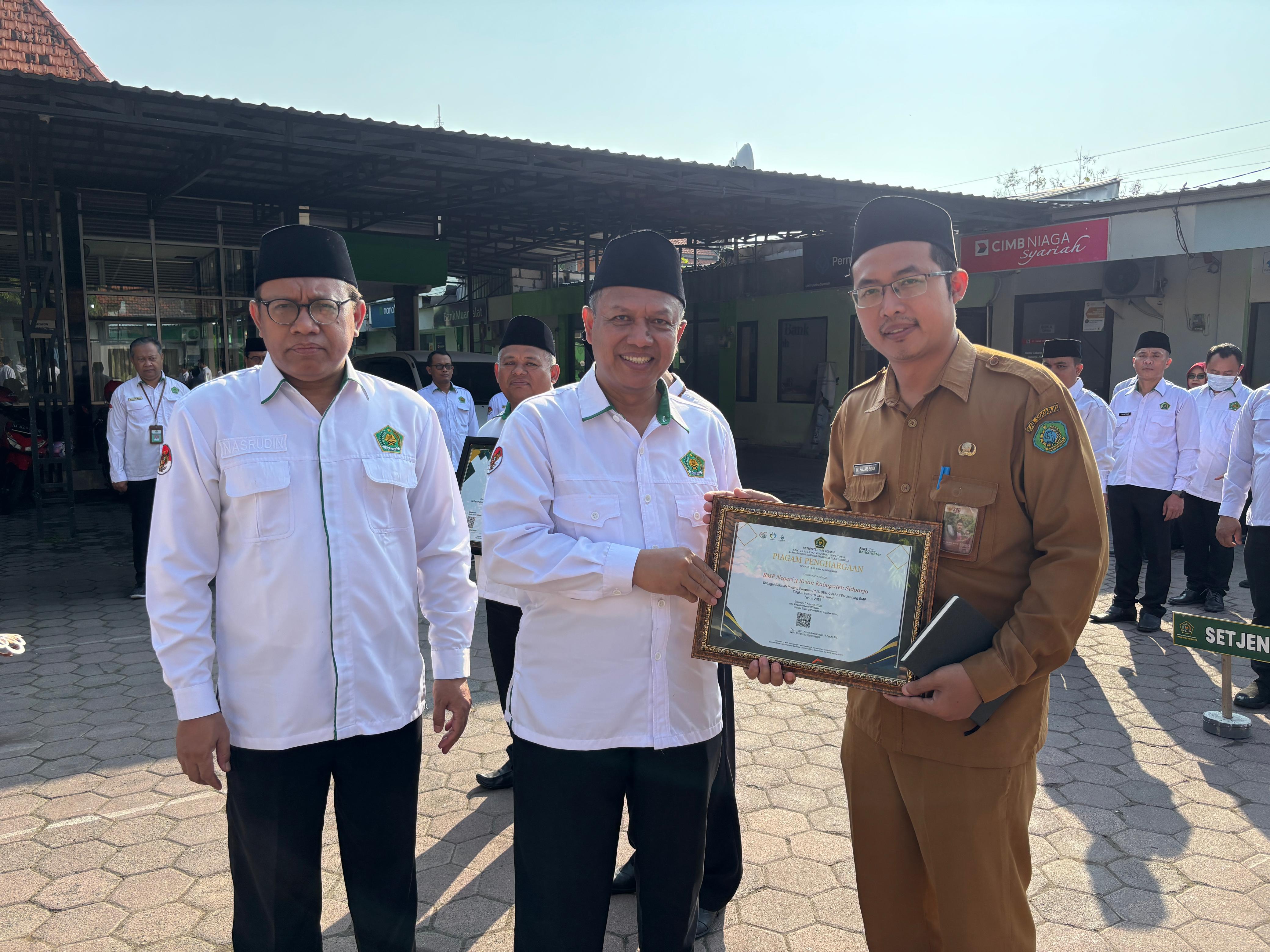 LUAR BIASA: Kepala SMPN 3 Krian, M. Fajar Sidik, S.Pd.I., M.Pd. (kanan) menerima penghargaan sebagai sekolah piloting Program PAIS Berkarakter jenjang SMP tingkat Jatim 2025. (ANAS/RADAR SIDOARJO)