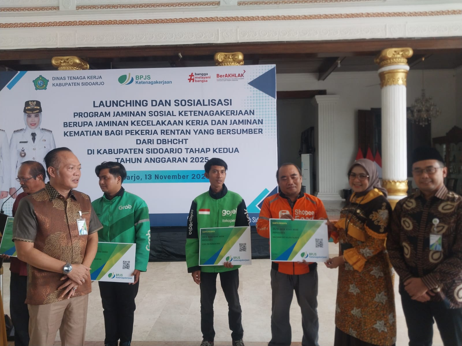 PEDULI: Kepala Disnaker Sidoarjo Ainun Amalia (dua dari kanan) menyerahkan bantuan jaminan sosial ketenagakerjaan ke driver Ojol, di Pendapa Delta Wibawa, Kamis (13/11/2025).