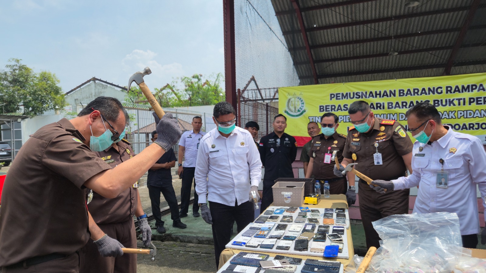 BARANG BUKTI: Petugas menghancurkan ponsel menggunakan palu.