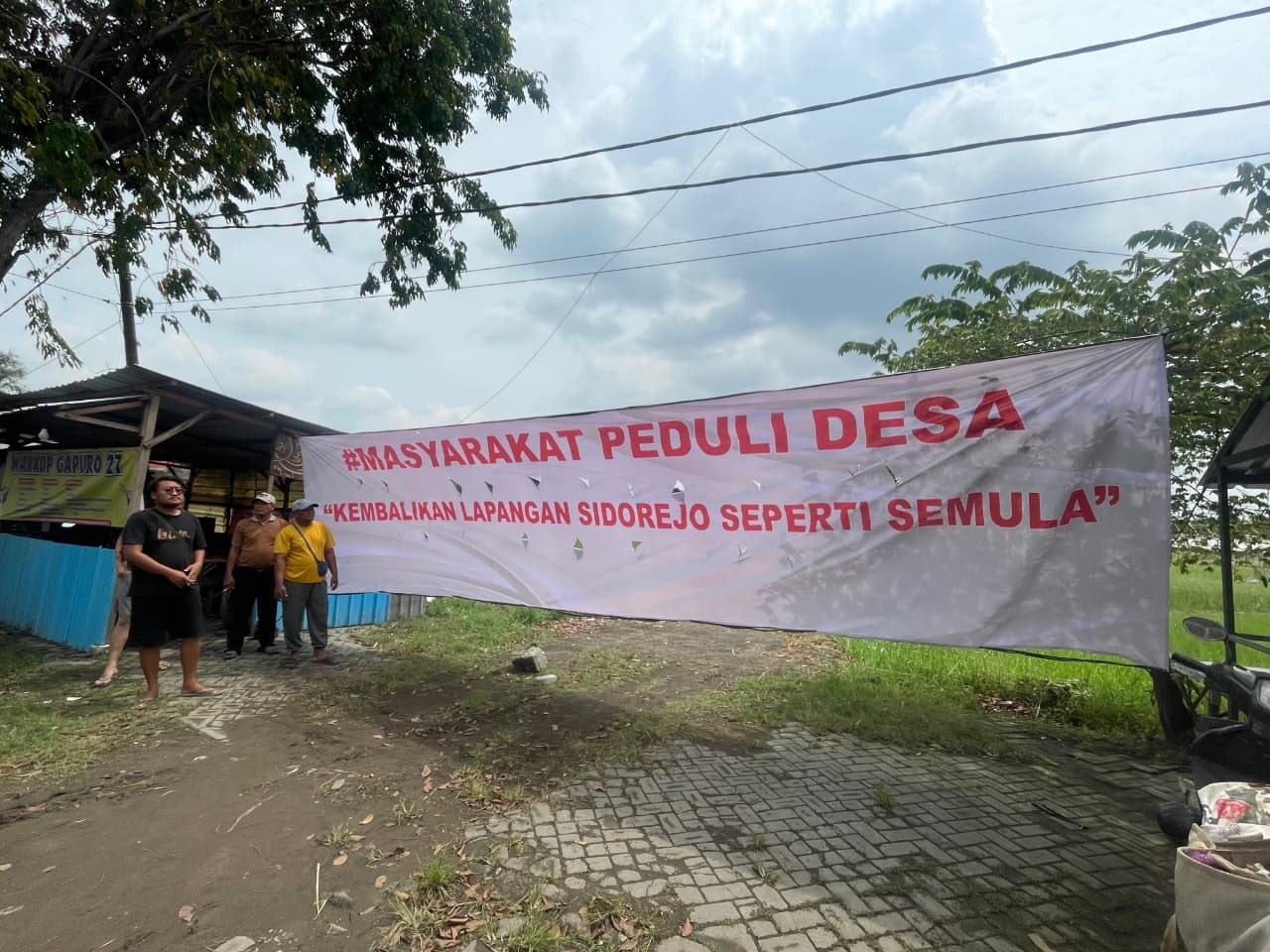 KECEWA: Warga membentangkan spanduk penolakan penggunaan lapangan desa sebagai lokasi Koperasi Desa Merah Putih di Desa Sidorejo, Kecamatan Krian, Minggu (11/1). (DIKY SANSIRI/RADAR SIDOARJO)