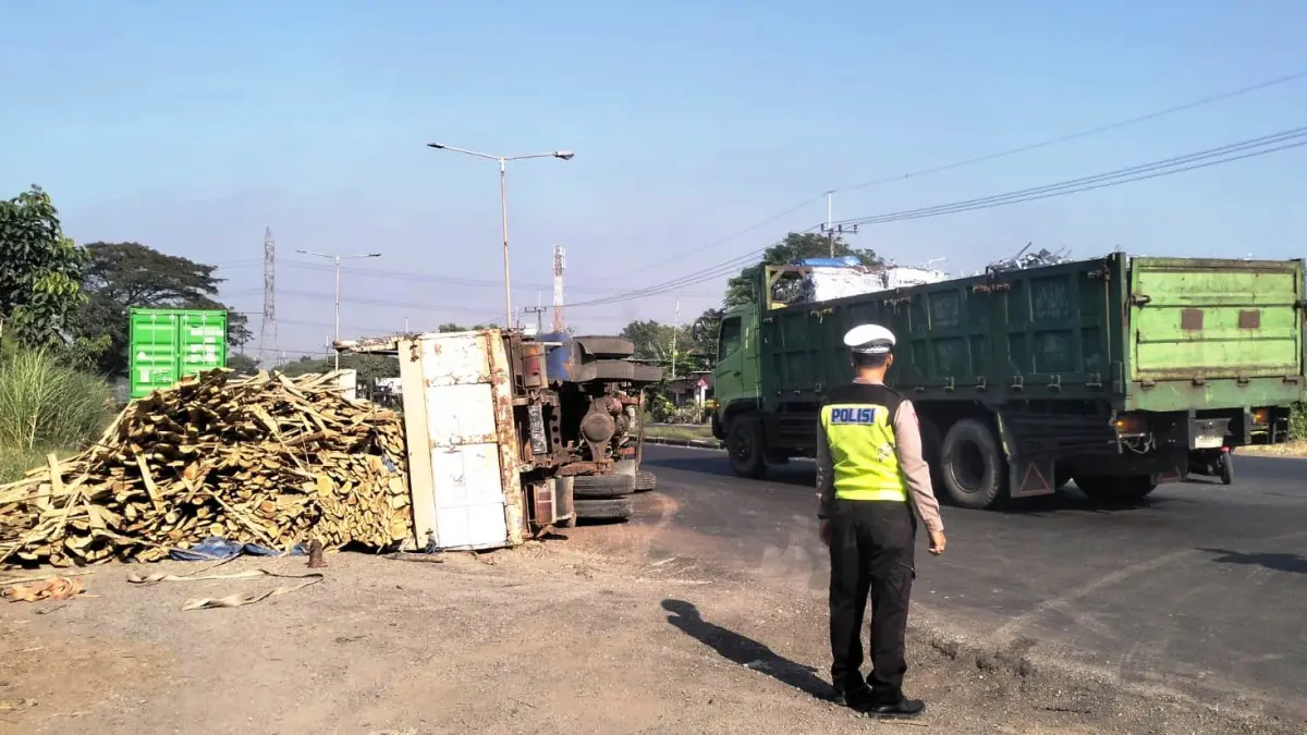KECELAKAAN: Kondisi truk bermuatan kayu yang terguling di Jalan Raya Bypass Krian, Sidoarjo, Jumat (3/7).