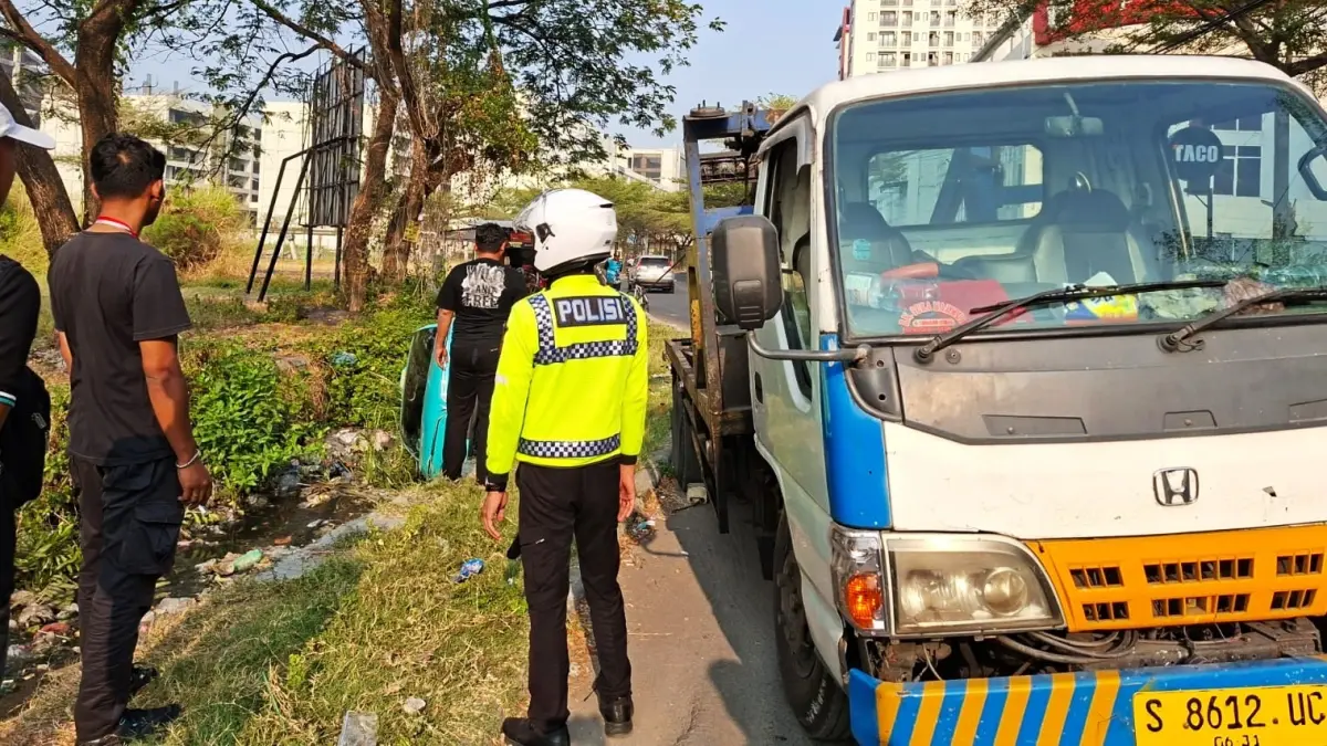 KECELAKAAN: Petugas berusaha mengevakuasi taksi listrik yang masuk saluran air.