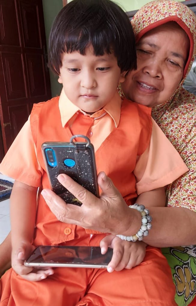 MENYENANGKAN: Sambil dipangku, Muhammad Hafiz Khalif Al-Khoir mengikuti MPLS dari layar handphone. (RIZKY PUTRI PRATIMI/RADAR SIDOARJO)