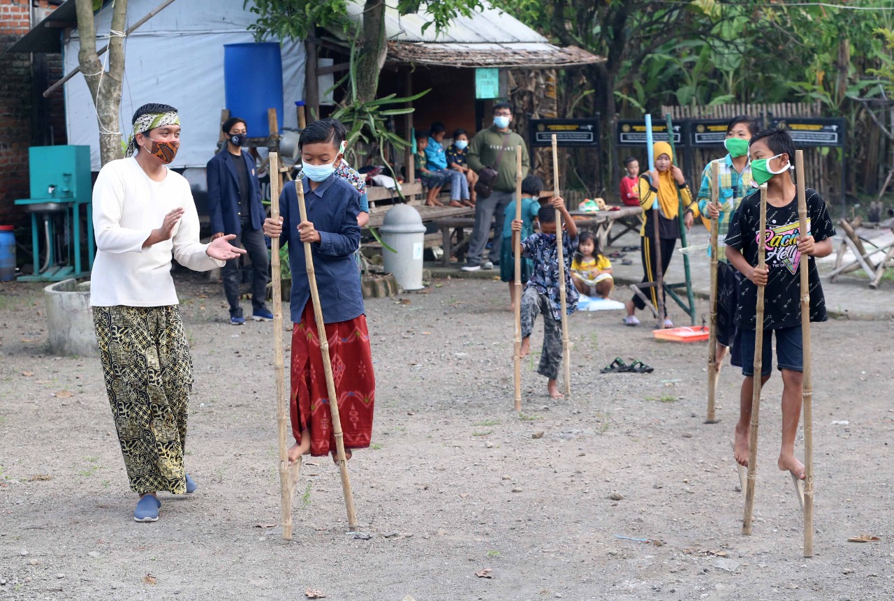 PERKUAT IMUN: Ahmad Irfandi (kiri) anggota komunitas Sidoasik mengajari anak-anak di Desa Pagerngumbuk, Wonoayu bermain egrang. (RIZKY PUTRI PRATIMI/RADAR SIDOARJO)