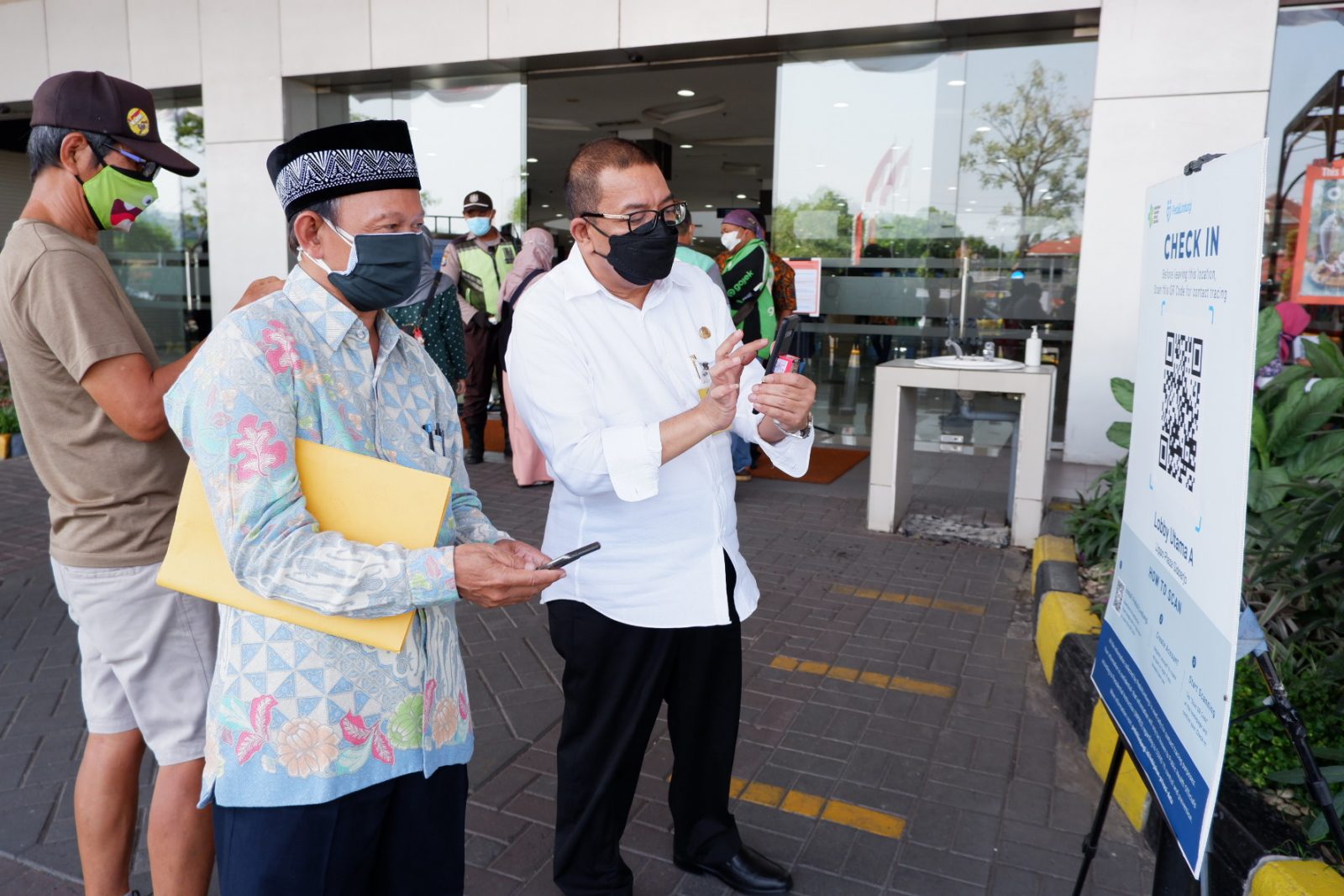 PROKES: Kepala Disperindag Sidoarjo Tjarda (kanan) membantu pengunjung mal yang kesulitan mengakses aplikasi Peduli Lindungi. (RIZKY PUTRI PRATIMI/RADAR SIDOARJO)