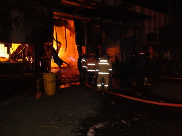 SULIT DIJINAKKAN: Petugas PMK lakukan pembasahan di lokasi gudang yang terbakar.