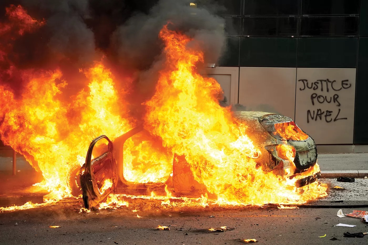 Sebuah mobil terbakar di dekat tembok yang bertuliskan gratifi, "Keadilan untuk Nahel" di Nantere, Kamis (29/6). Kerusuhan terjadi karena kemarahan penduduk atas pembunuhan remaja.