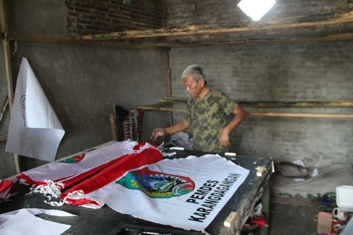 Alfan Efendi, 75, warga Kelurahan Kaliwungu, mengebut pesanan bendera dan umbul-umbul di rumahnya.