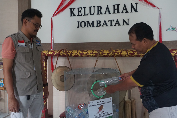 Indra Pratama SSTP (kiri) Kepala Kelurahan Jombatan mendampingi warga yang memasukkan botol plastik ke tempat yang disediakan.