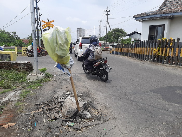 Jalan di depan perlintasan KA sebidang di Desa Sembung, Kecamatan Perak, Jombang yang rusak ditandai dengan bambu dan kresek, Sabtu (2/12).