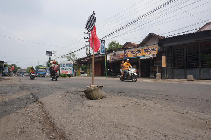 Jalan kabupaten di Desa Selorejo, Kecamatan Mojowarno, yang rusak ditandai dengan memasang pot bunga karena membahayakan pengguna jalan, Jumat (29/12).