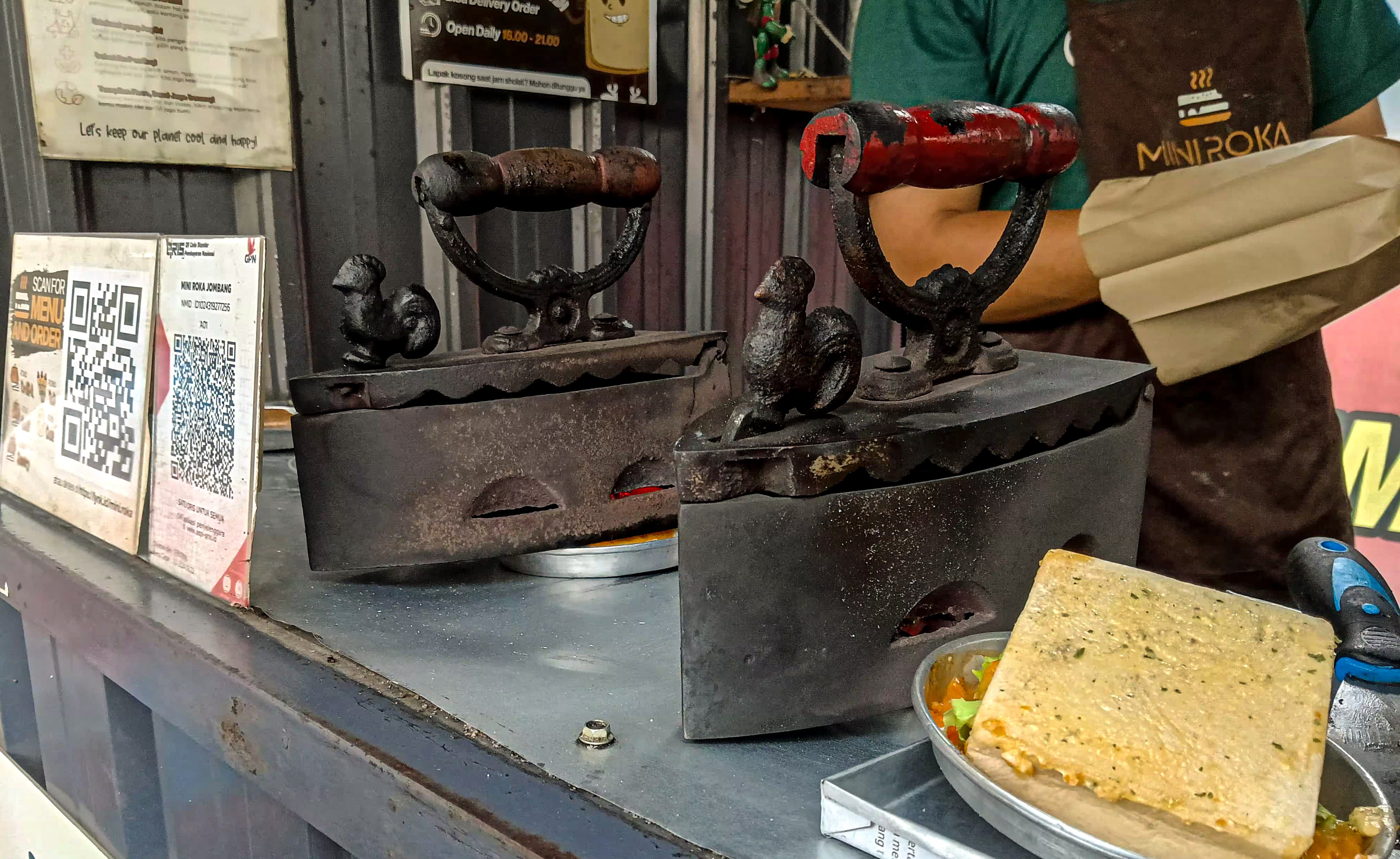 Proses pembuatan roti bakar menggunakan sertika arang jadul di salah satu kedai di Jombang