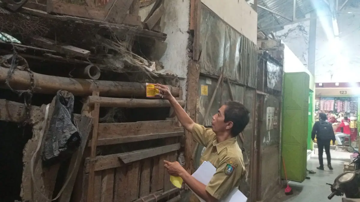 DISEGEL: Petugas menempel stiker segel di kios Pasar Mojoagung, Selasa (1/8).