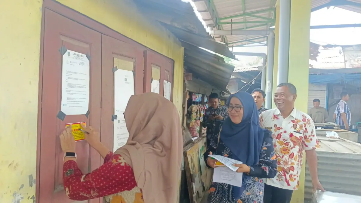 DISEGEL: Petugas memasang stiker segel di salah satu kios Pasar Sumobito yang mangkrak dan menunggak retribusi, Kamis (3/9).