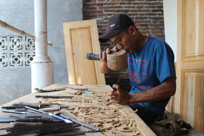 Eko Winiarto, sedang menyelesaikan pesanan ukiran pintu di rumah pemesannya.