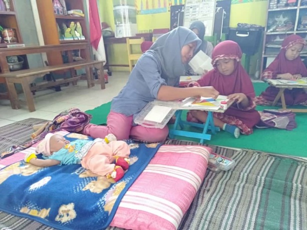 siswa TK Negeri Pembina, Desa Wangkalkepuh, Kecamatan Gudo mengerjakan Tangram didampingi ibu yang membawa anak bayinya.