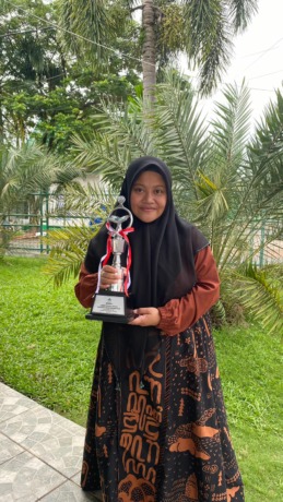 Ummu Habibah menenteng piala juara 1 tafsir Bahasa Inggris MTQ Nasional di Banjarmasin 13-19 Oktober 2022.