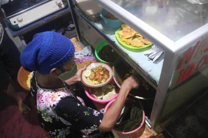 Supiyati, sedang meracik nasi kuning pesanan pelanggan di warung yang berada di dapur rumahnya.