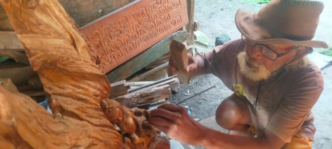 Soedirman sedang membuat hiasan dinding kaligrafi dari kayu bekas di rumahnya.