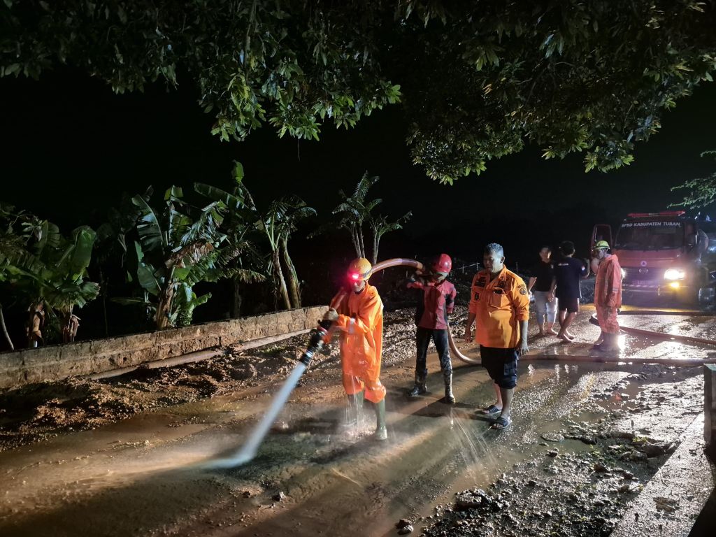 Petugas BPBD bersama warga menyapu jalan yang dipenuhi lumpur karena banjir bandang.