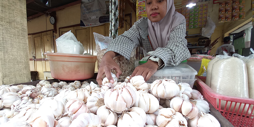 Penjual bahan pokok di Pasar Baru Tuban tengah mengambil bawang putih untuk ditimbang.